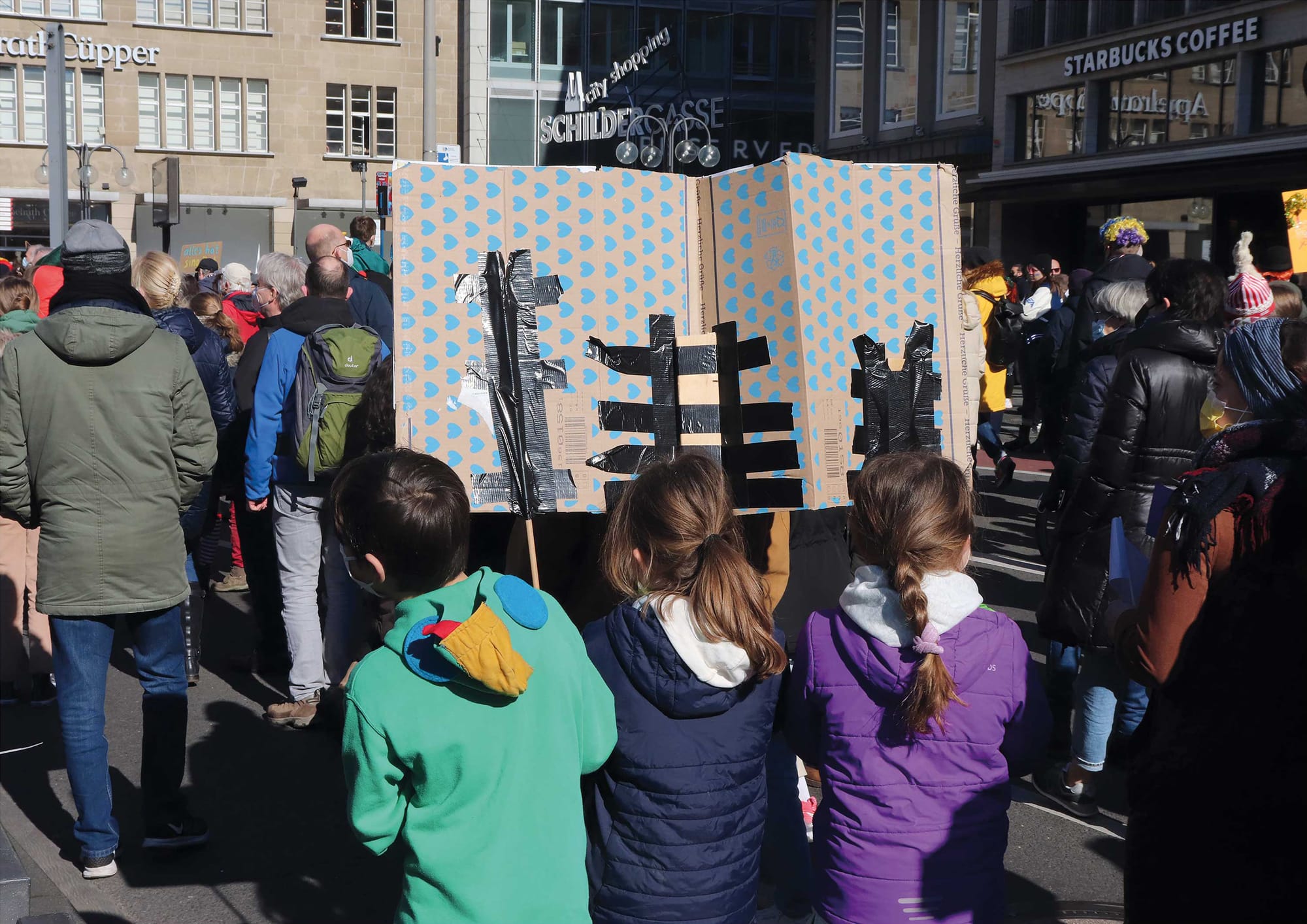 Drei Kinder mit einem selbst gebastelten Plakat von hinten